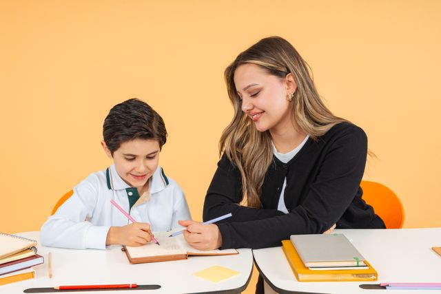 Inscription Young teacher helps a schoolboy with writing at a desk, fostering learning.