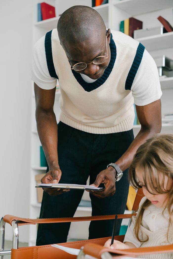 Accueil An adult assisting a young girl with schoolwork in a classroom setting.