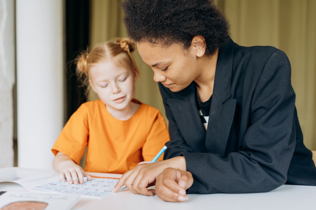 Mother helping daughter with homework at home in warm daylight.